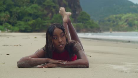 a young trinidadian girl lays in the sand on a tropical beach in trinidad wearing a bikini