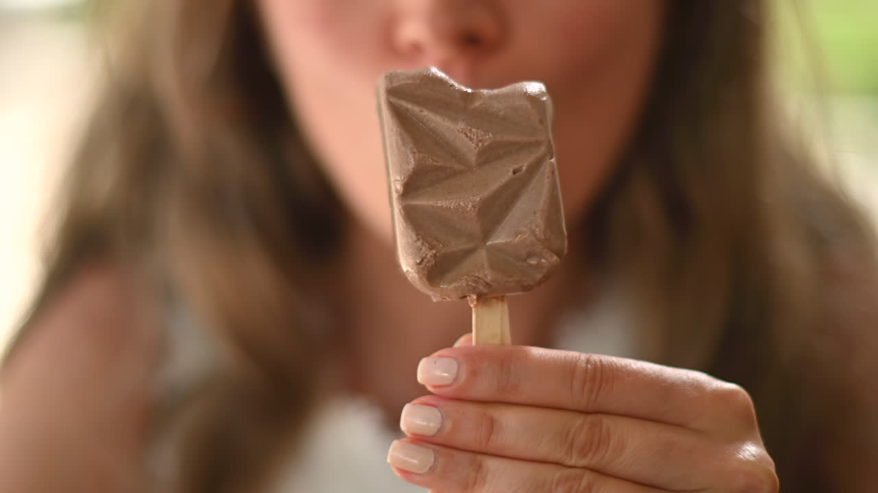 Donna bruna che mangia un gelato rosa in un bar, alla luce del giorno