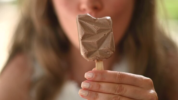 Donna bruna che mangia un gelato rosa in un bar, alla luce del giorno