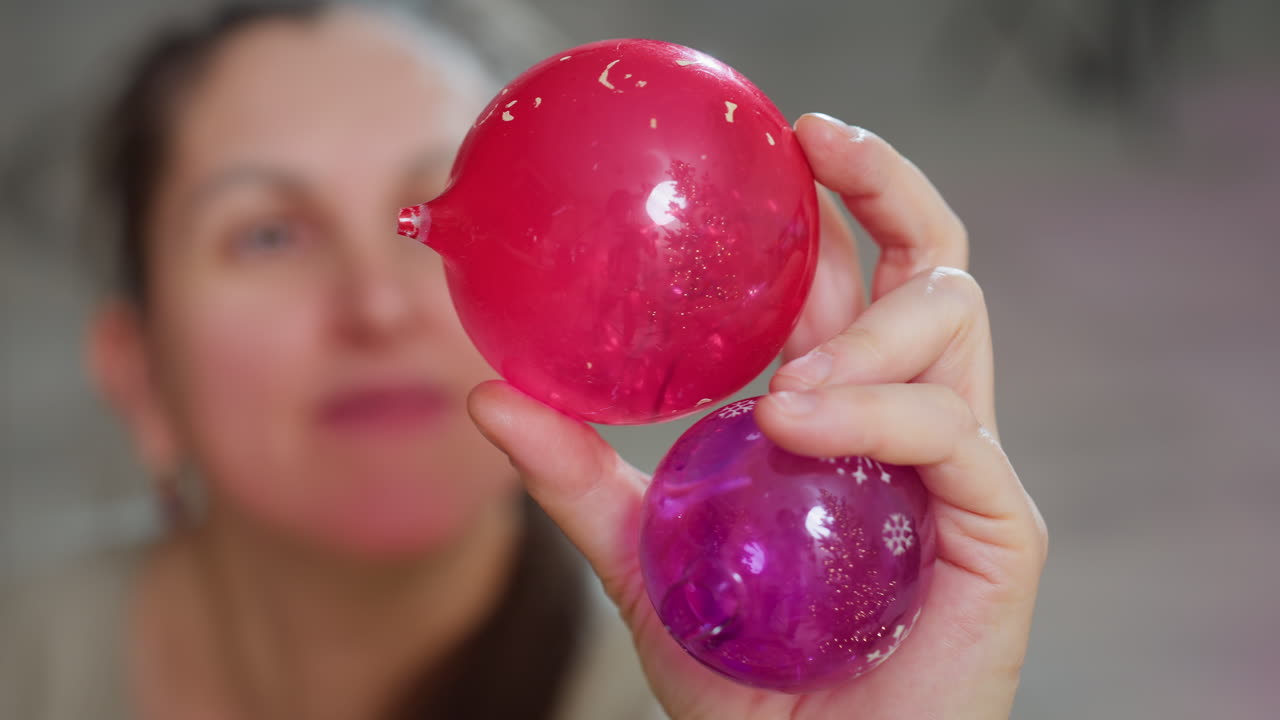Blurred view of woman in festive mood holding vibrant red and purple ornaments close to camera, focusing on colorful holiday decorations with joyful atmosphere and soft background ambiance