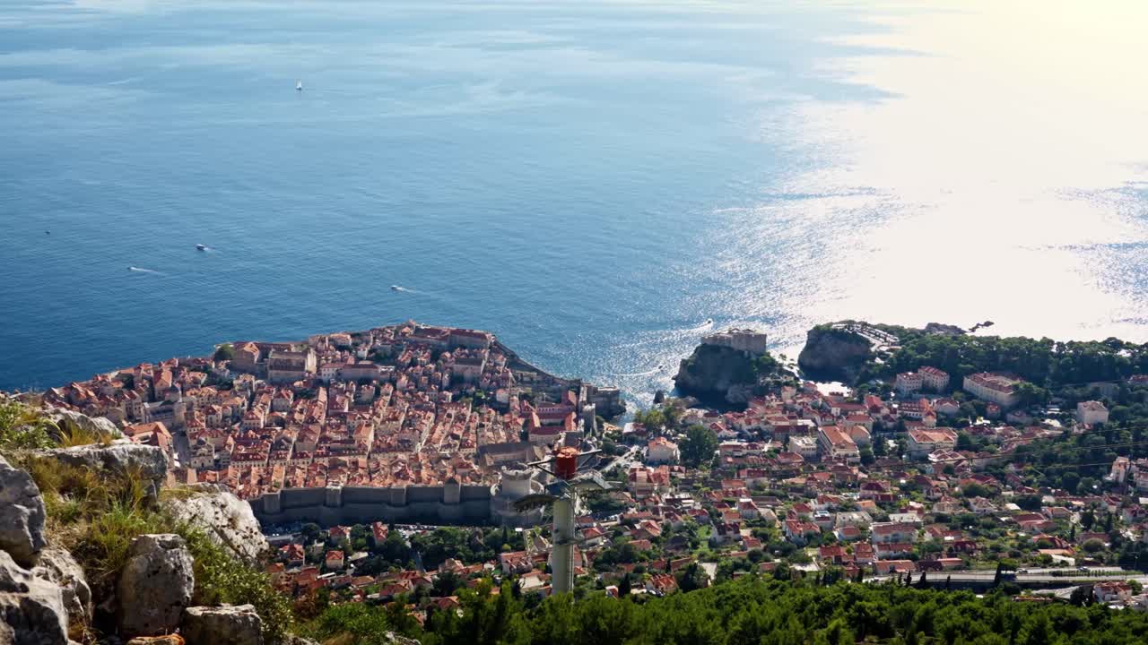 Landscape panning view from Dubrovnik’s Old Town toward the wider city, revealing terracotta-red roof houses, historic streets, and the deep blue Adriatic Sea stretching along the scenic Mediterranean