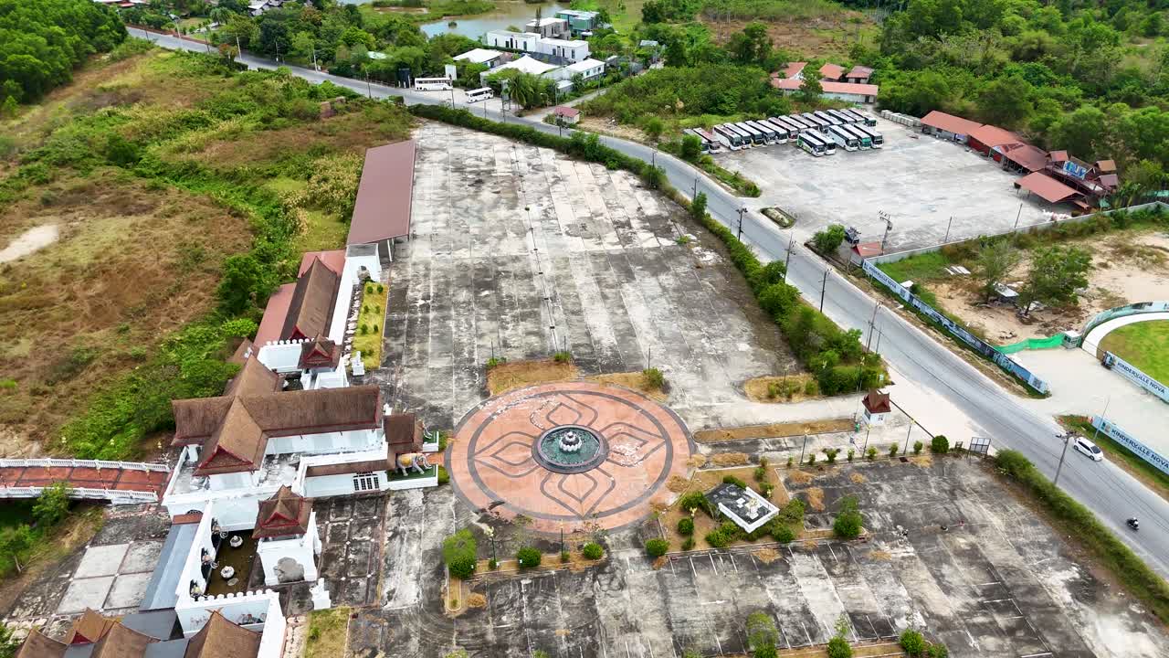 Drone footage captures a serene Buddhist temple in Phuket, Thailand, showcasing its architecture and surrounding greenery in natural daylight