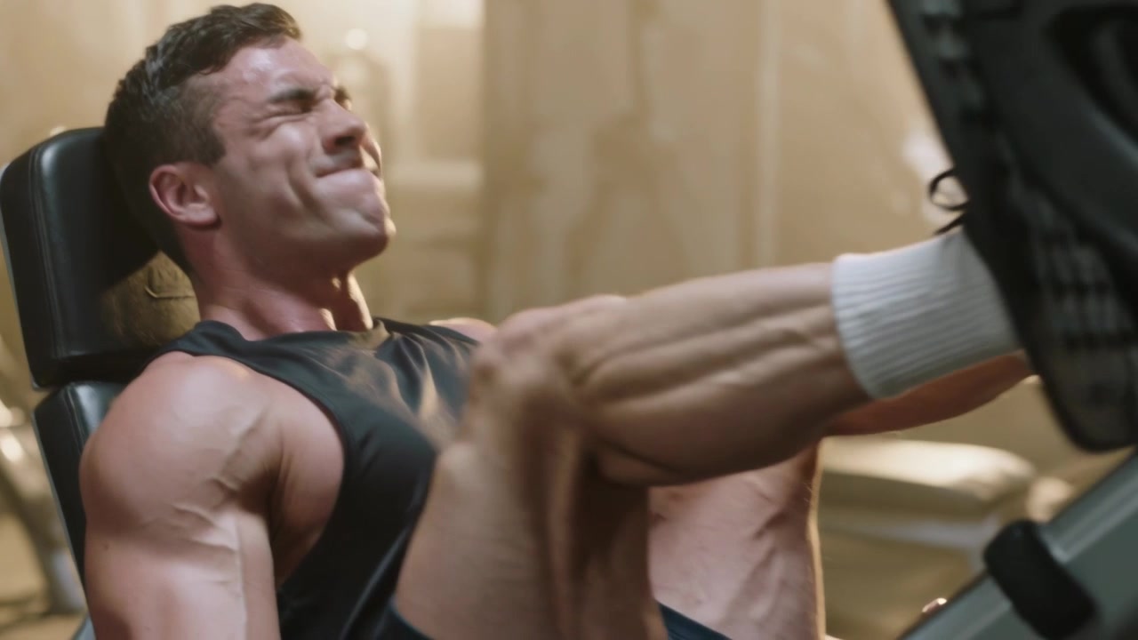 Iniciando o empurrão, homem adulto vestindo regata preta realizando leg press com anilhas na academia, repetindo as pressões.
