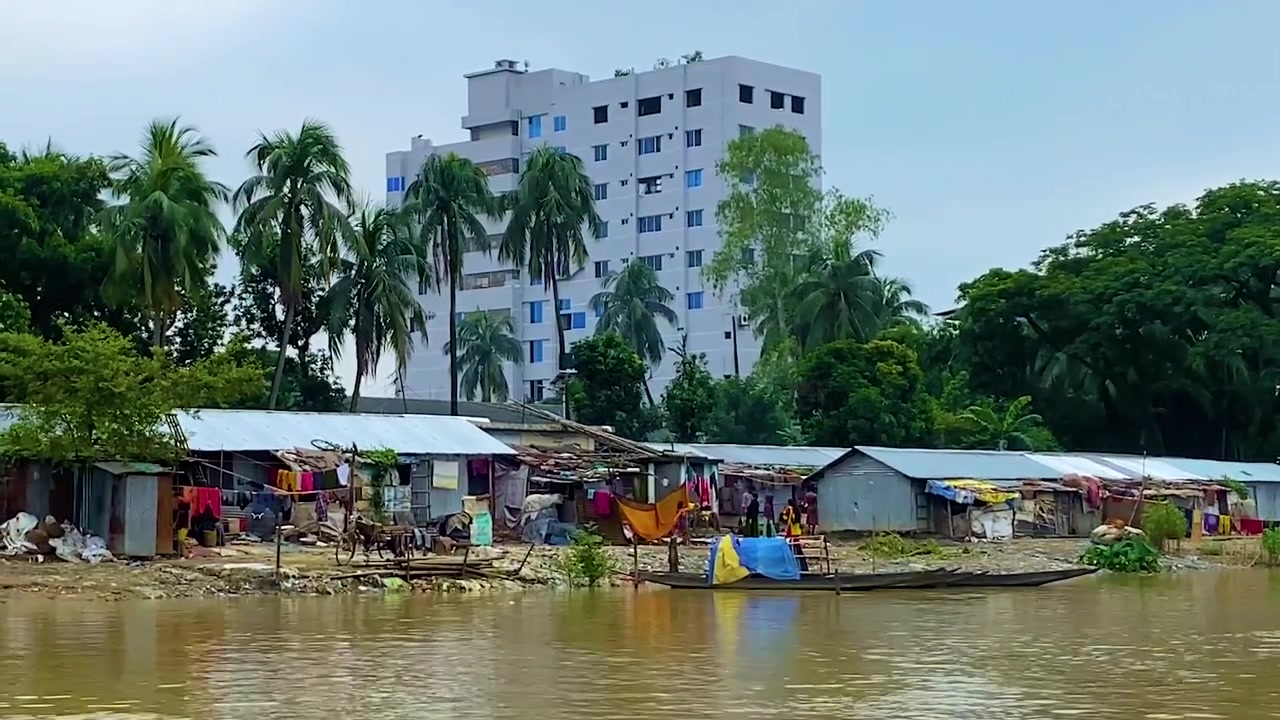 Realtà Ricchi vs Poveri: Insediamento di baraccopoli lungo il fiume accanto a un edificio moderno. Estrema disuguaglianza sociale in Bangladesh