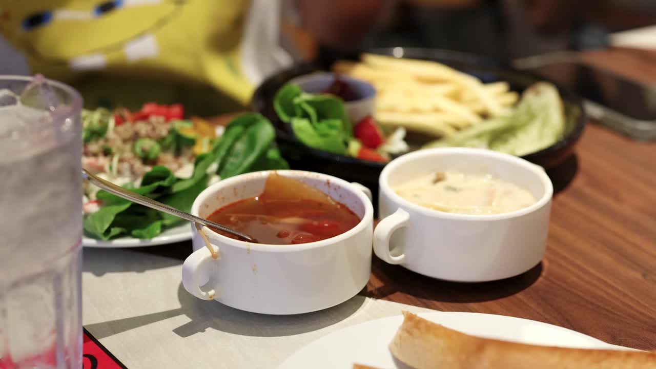 Diner enjoys salad, red soup, creamy soup, fries, and water in bright restaurant lighting