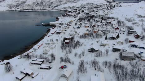 vista de avión no tripulado en el área de tromsø en invierno volando sobre un pueblo nevado con casas de madera y el océano en el lado en noruega