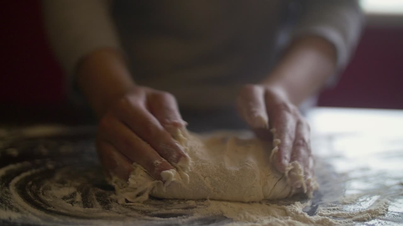 Woman's hands making pizza dough on a marble table full of flour