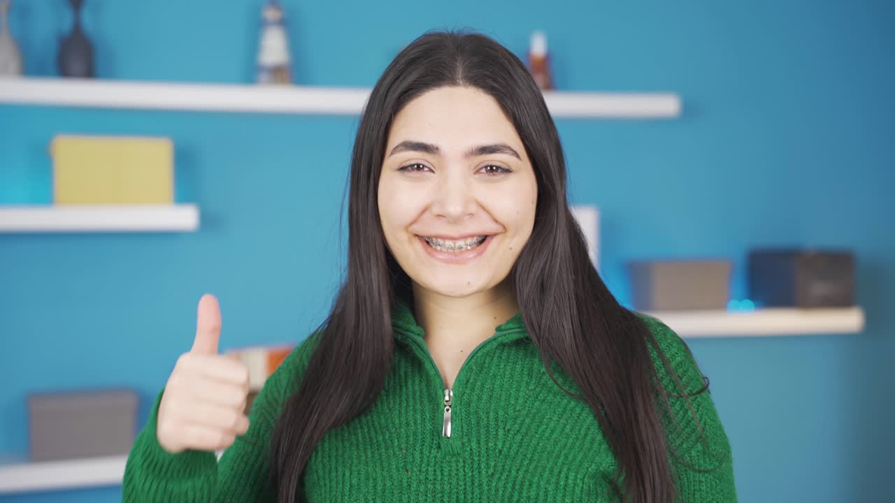 una mujer joven con aparatos ortopédicos mira a la cámara, hace una señal de "sí" y sonríe.