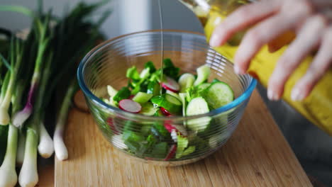 woman hands pouring olive oil into glass bowl with fresh spring salad