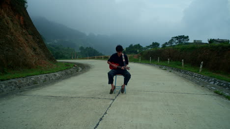 musician sitting in the middle of a quiet road playing his ukulele
