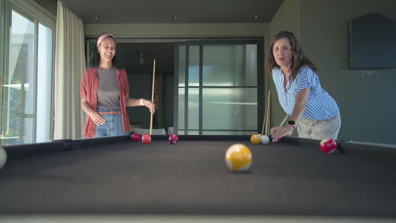 Diverse amiche che giocano a biliardo in una sala ricreativa, osservando la donna a destra che colpisce la palla gialla sul panno nero.
