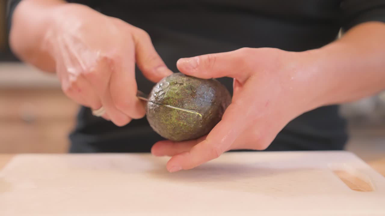 An at-home cook cuts an avocado in half using a chef's knife.