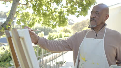 happy senior biracial man painting at balcony at home, slow motion