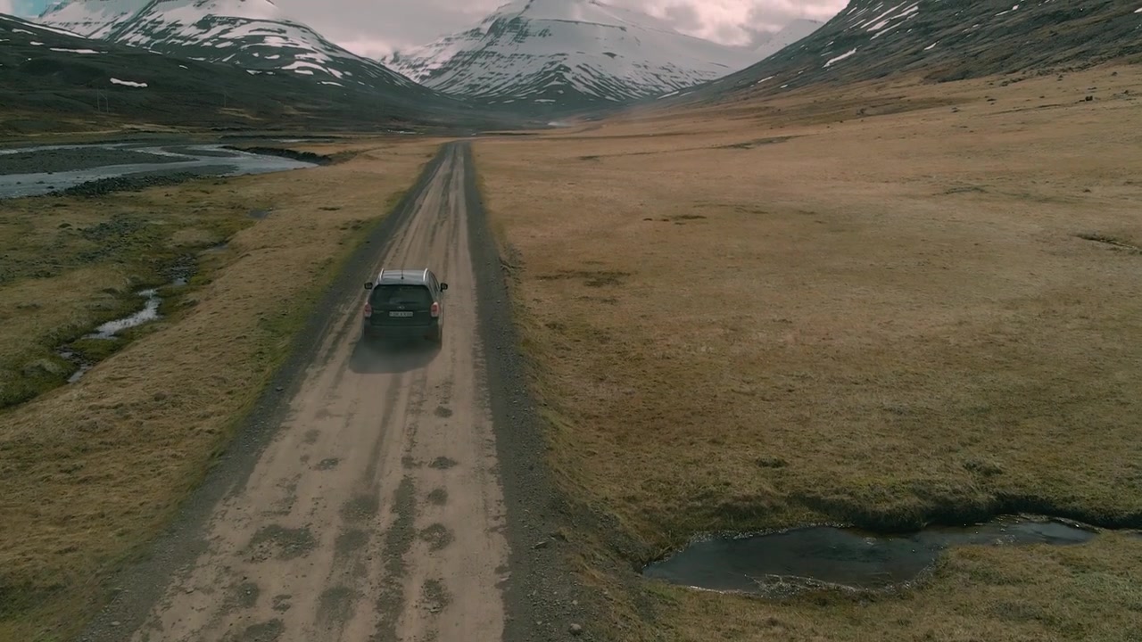 Vista aerea di un SUV che percorre una strada sterrata in una valle montana islandese