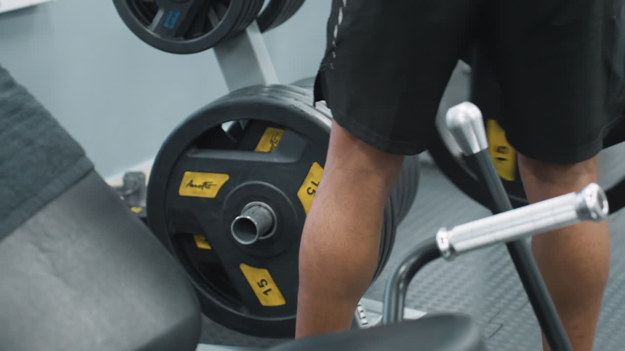 Gym attendant placing weight plate back onto barbell rack on rubber gym flooring, showing focused hands guiding heavy iron plate into position during equipment