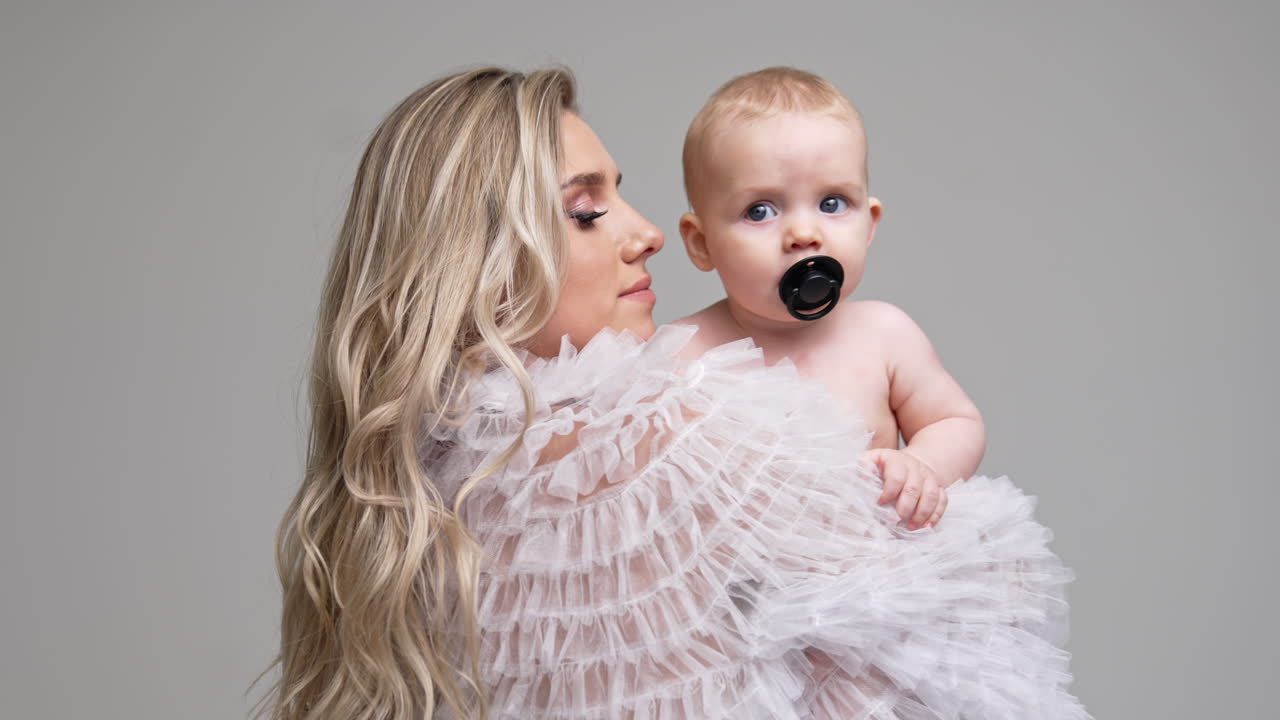Caucasian woman stands her back to camera holding a baby. Little infant in mom's hands having a pacifier in mouth.