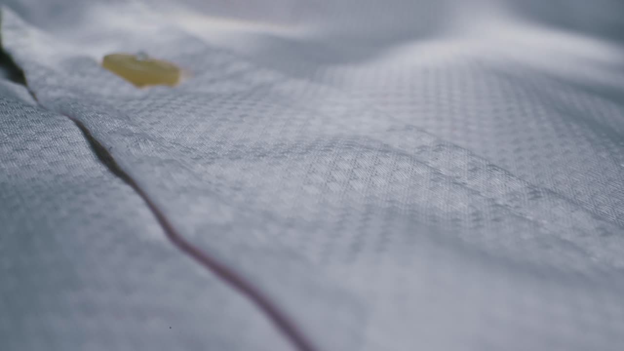 This is a detailed closeup view of a classic white shirt showcasing its button and the beautifully textured fabric