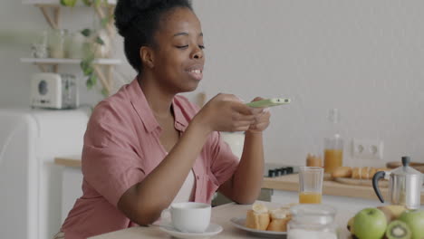 woman using phone while eating breakfast in kitchen
