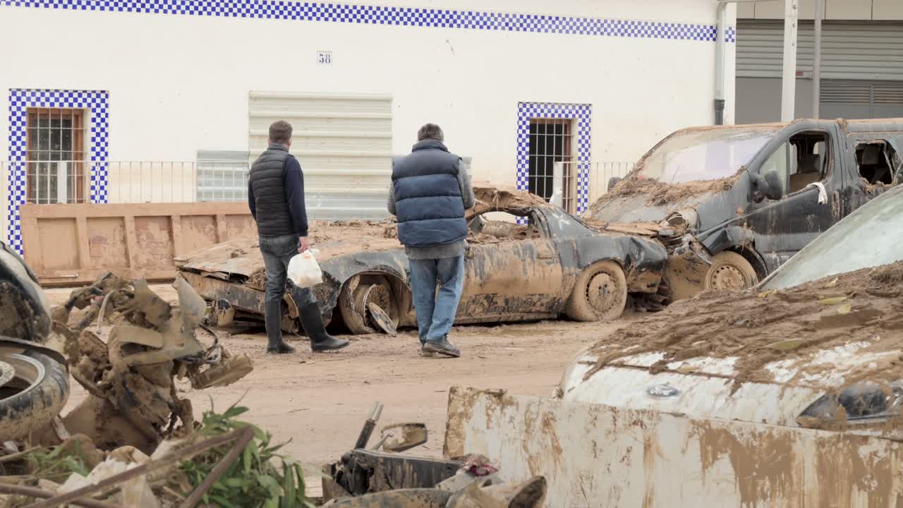 People inspecting severe flood damage to a car in Valencia, Spain
