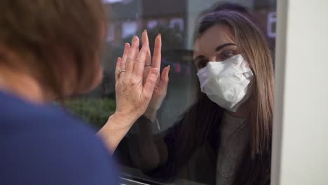 young lady looking at grandmother through the window during covid-19 outbreak