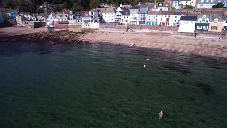 Menschen,-Die-In-Kingsand-In-Torpoint-Schwimmen,-Mit-Einer-Luftaufnahme-Einer-Drohne,-Die-Sich-Nach-Oben-Neigt-Und-Das-Dorf-Enthüllt