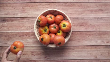 mano alcanzando una canasta de tomates en una mesa de madera