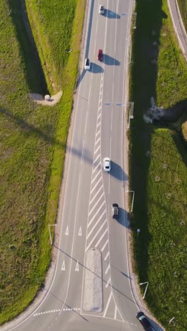vertical drone flies above katlakalns interchange where daugmale road splits at the roundabout, showing road markings, traffic signs, and vehicles circulating in spring countryside