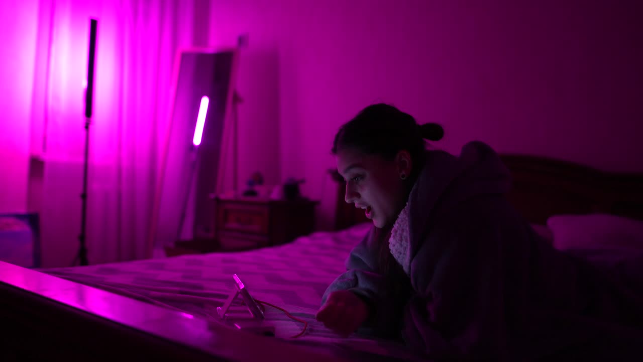 Donna che guarda una videochiamata sul telefono in una camera da letto illuminata di rosa di notte