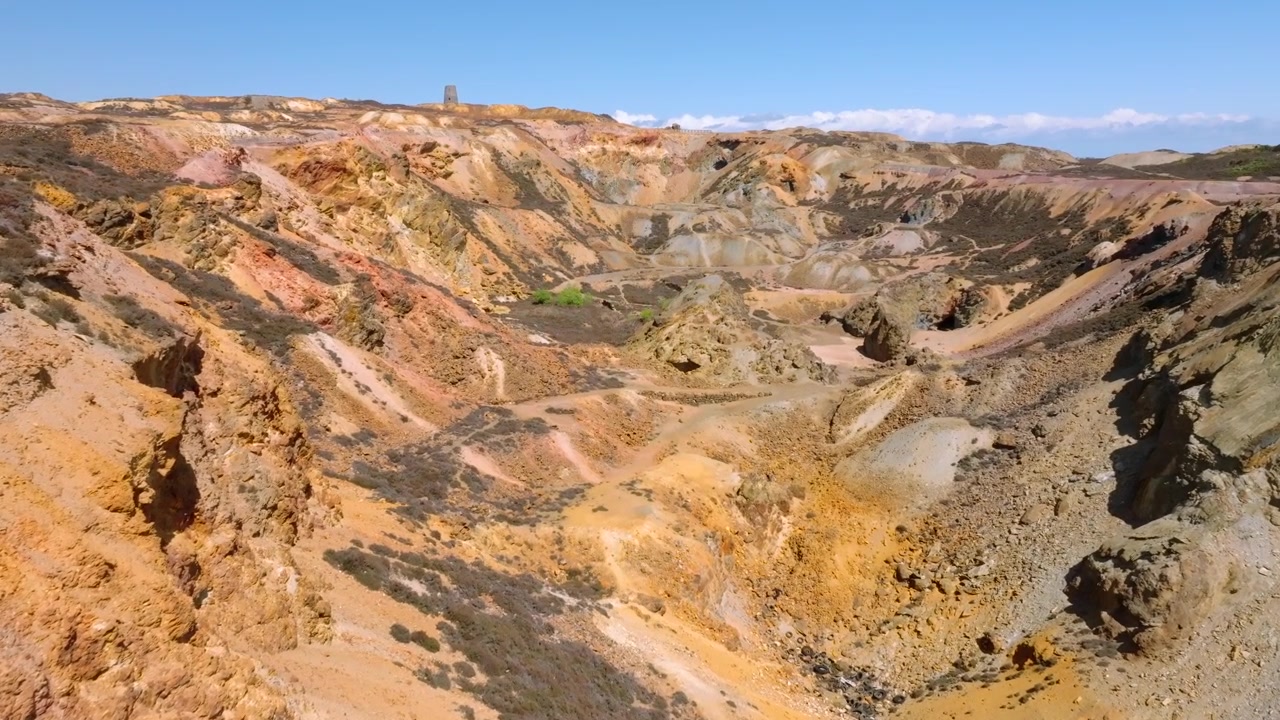 Parys Mountain Copper Mine, Amlwych, Anglesey, Wales, UK. Drone flight over cliff edge and over deep main mineralised crater towards distant derelict hilltop windmill.