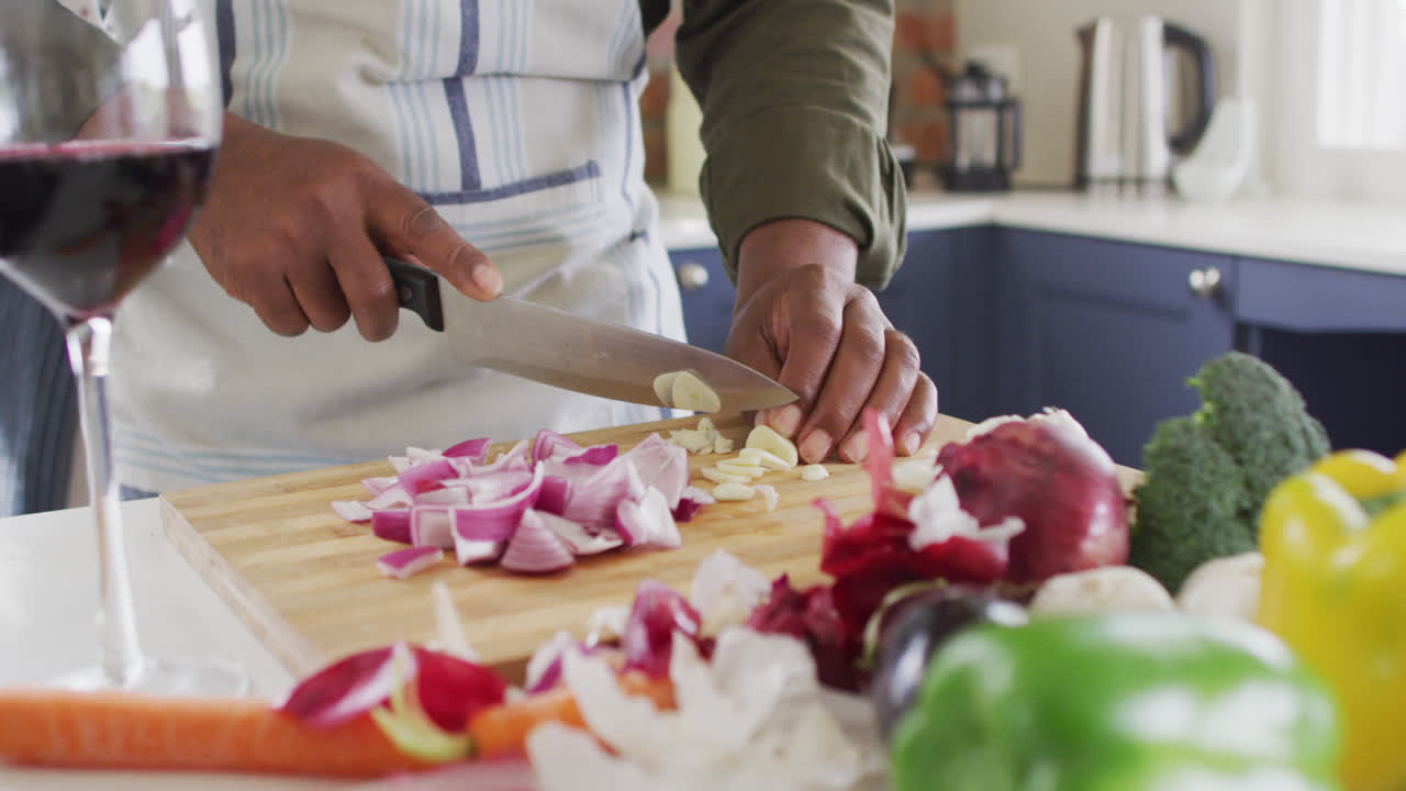Mid section of man wearing apron chopping vegetables in the kitchen at home