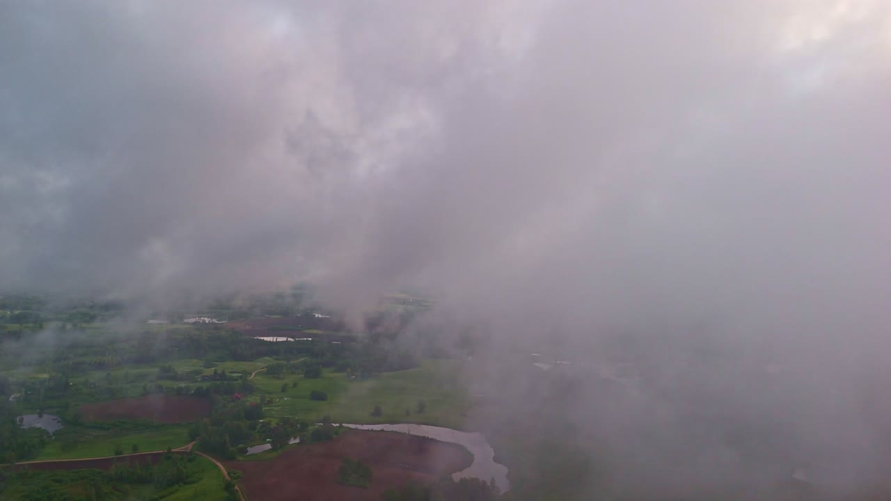 Dramatische omgekeerde luchtvlucht die opkomt uit dikke wolken om een uitgestrekt, groen platteland te onthullen.