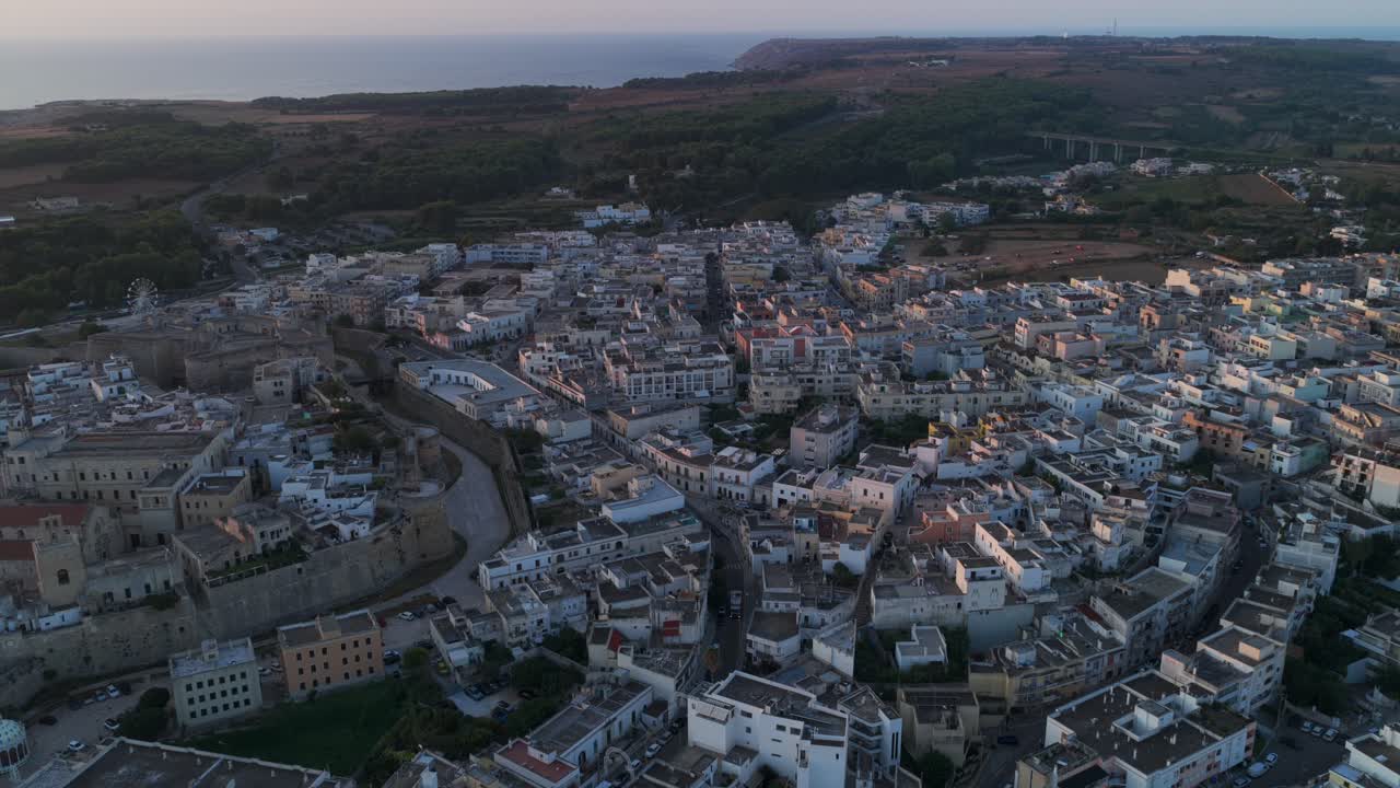Historic center of Otranto, Puglia, at dusk, Aragonese Castle, cathedral, town with sea in background, Italy. Aerial backward