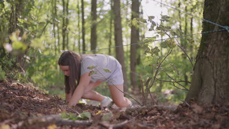 children in a summer camp hike crawls on the ground. training of passing obstacles by crawling on the ground. a girl tumbles in the forest on a camp assignment