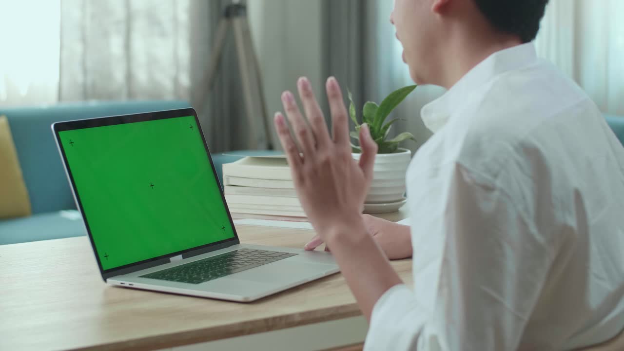 Close Up Of Asian Man Student Raises Hand And Asks A Question While Using Green Screen Computer At Home