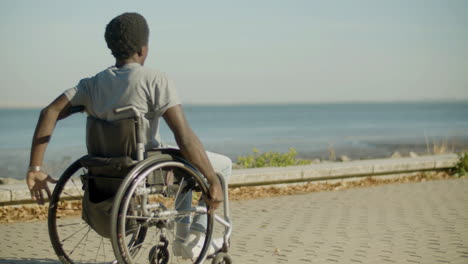 young black man in wheelchair riding along seafront road