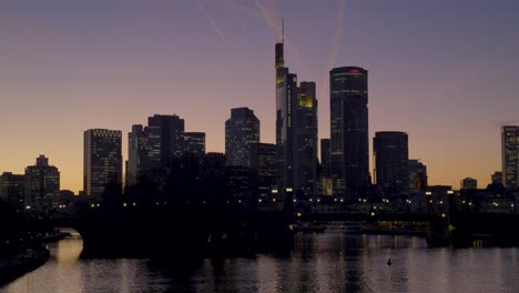 urban skyline of frankfurt, germany with skyscrapers lit up at sunset over river