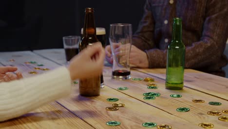 close up of friends at home or in bar celebrating at st patrick's day party drinking alcohol and playing with novelty gold coins