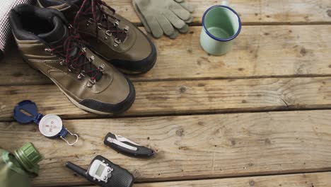 camping equipment with boots, gloves and compass and copy space on wooden background