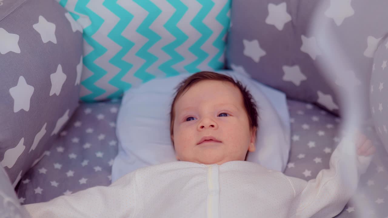 귀여운 아기가 아름다운 편안한 침대에 누워서 주위를 둘러보고 있습니다. 카메라의 원형 움직임.