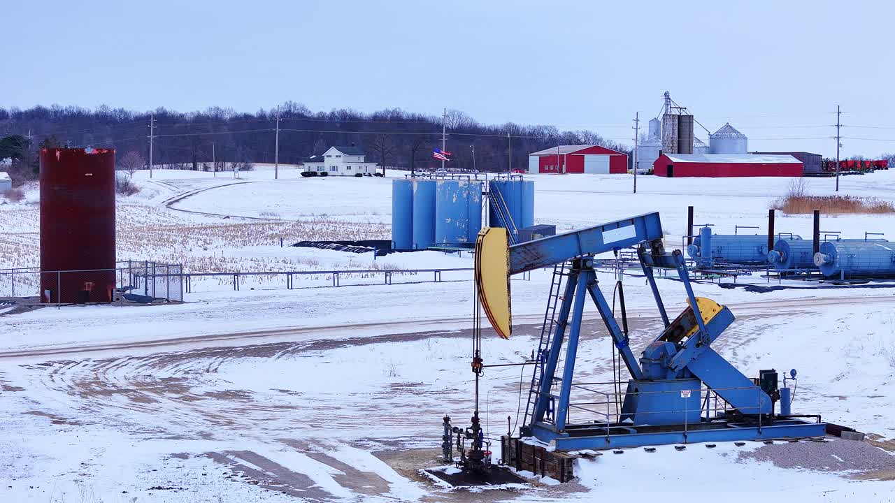 Oil pumpjack operating in winter field, extracting fossil fuels for energy, southeast Michigan, USA in aerial view