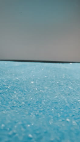 Bright blue sand crystals lie in thin layer on loud speaker. Device rotates and diaphragm moves lifting decorative loose materials in room with gray walls macro