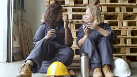 diverse workers talking, drinking coffee and eating cookies while sitting at wooden platform