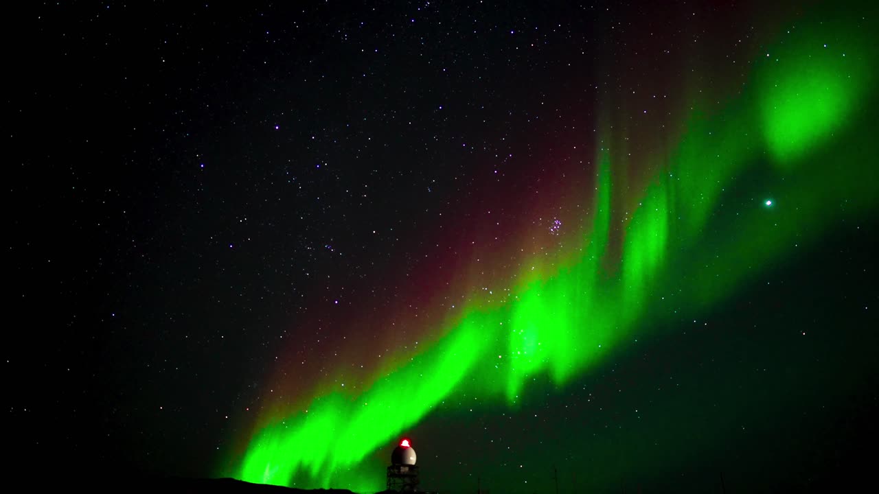 las luces del norte bailando entre las estrellas por encima de una torre lejana