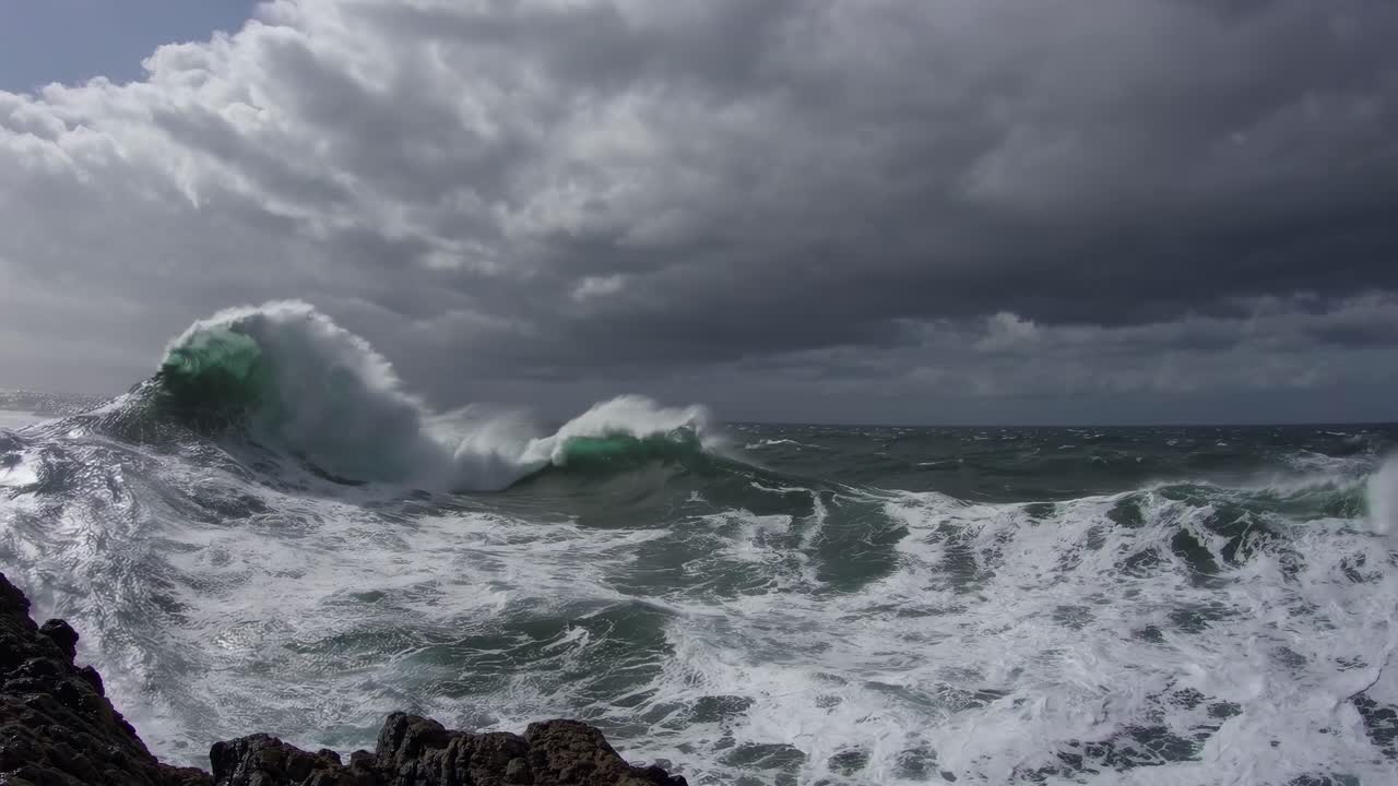 Dramatic wide-angle shot of stormy ocean waves crashing against rocks under dark clouds