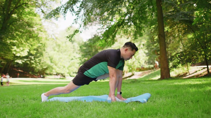 Asian man performs gymnastics stretching practicing yoga warrior pose on mat in urban city park