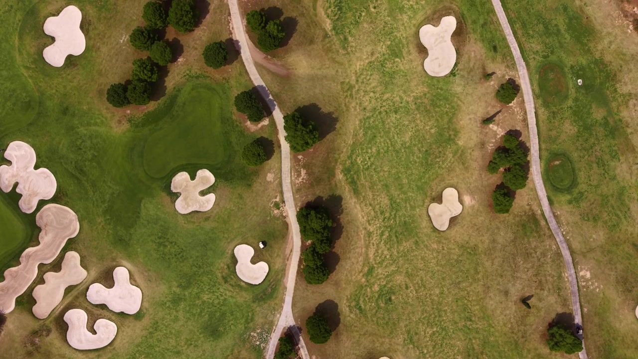 Top-down view of a golf course featuring sand bunkers, fairways, cart paths and scattered trees across manicured green grass