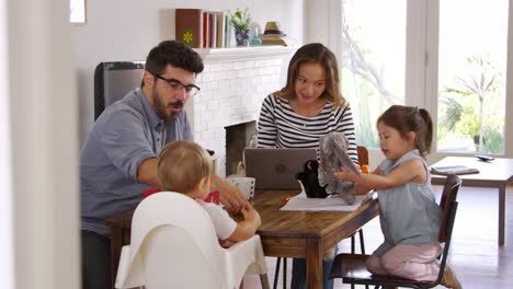 la madre usa la computadora portátil mientras el padre juega con los niños en casa