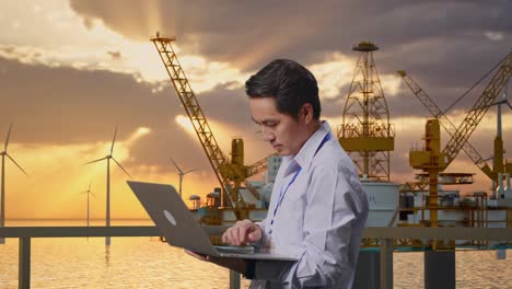 vista lateral de un trabajador profesional masculino asiático de pie con su computadora portátil con producción de hidrógeno en alta tecnología, instalación industrial, escribiendo en el teclado de su portátil con meditación