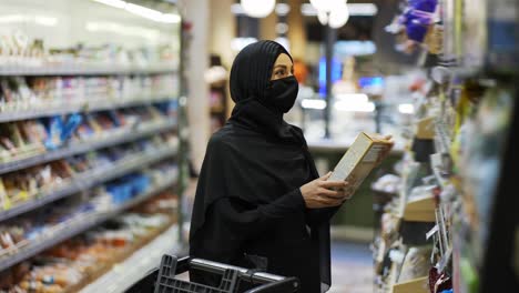 woman in hijab and protective mask doing grocery shopping in supermarket, choosing corn flakes