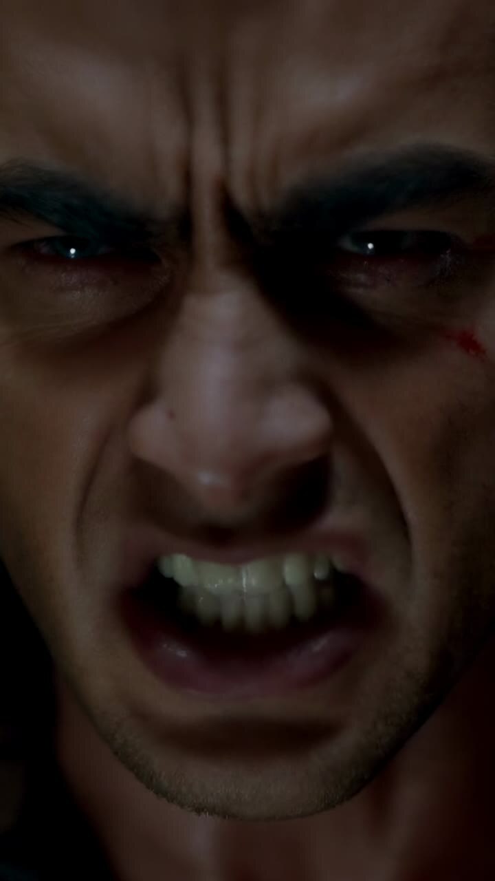 Vertical video: Opening with face filling shot, actor snarling, baring teeth in dim room, cheek cut